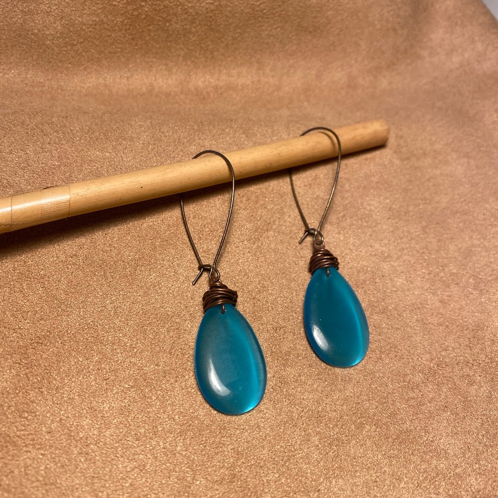 Peacock colored drop earrings with brass colored metal hoops.